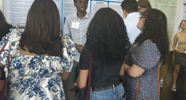 Student stands in front of poster while three attendees read poster