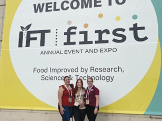 Three female students in front of IFT First conference sign