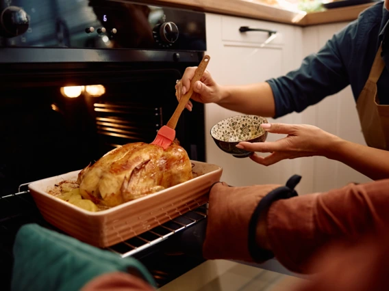Two people open the oven to baste a turkey