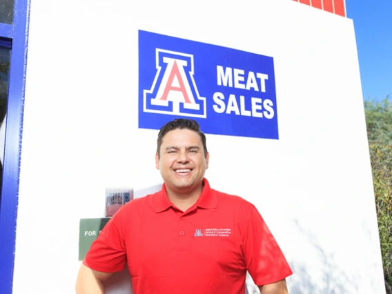 A man in a red shirt standing in front of a meat sales sign