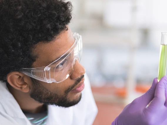 A male graduate student looking at fluid in a test tube in a lab